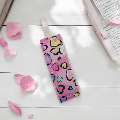 A pink bookmark with small and big hearts of various colours with a black surround. The bookmark has a pale pink ribbon loop attached.